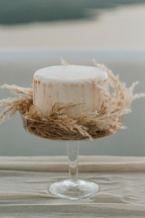 a neutral buttercream wedding cake with beige stripes surrounded with dried grasses is a stylish idea for a boho wedding