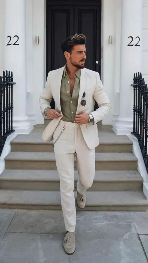 an effortlessly chic summer wedding guest look with an olive green shirt, a creamy linen suit, grey loafers and a chain