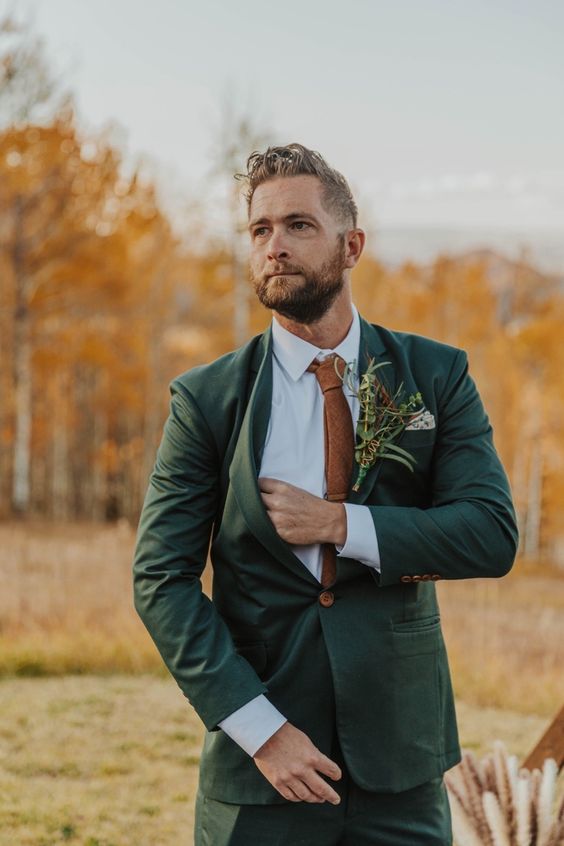 a bold green pantsuit, a white shirt, a brown tie and a lush greenery boutonniere are a cool combo for a fall wedding
