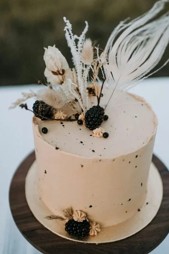 a neutral buttercream wedding cake with speckles, blackberries and dried blooms and grasses