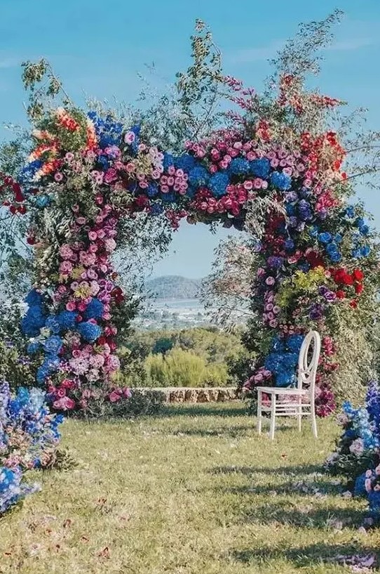 a super lush and bold floral wedding arch with blooming branches and flowers of all shades possible and with greenery