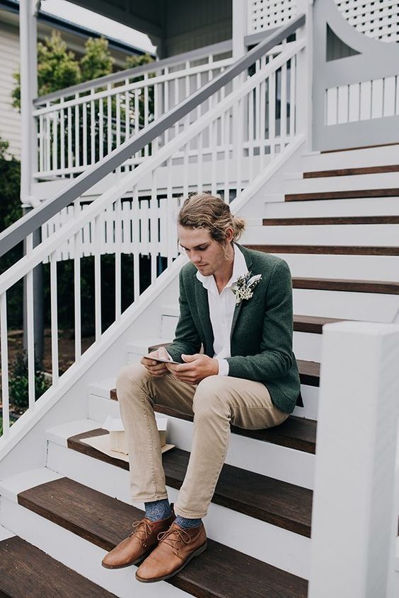 a casual and cool groom's outfit with a white shirt, neutral jeans, a green blazer, brown shoes and blue socks plus a boutonniere