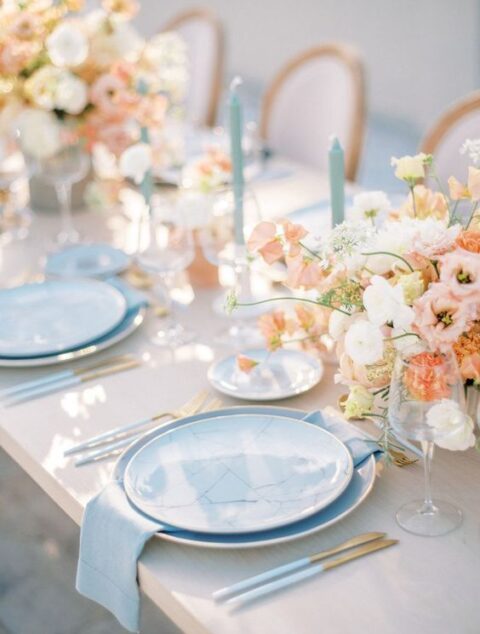 a delicate pastel wedding tablescape with blush and white blooms, blue marble plates and napkins, blue candles