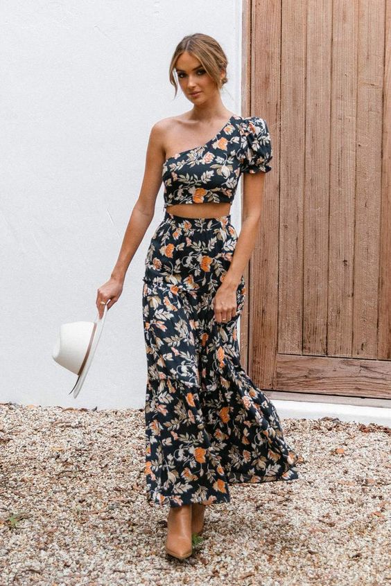 a chic black floral two-piece maxi dress with a one shoulder crop top, brown boots and a hat for a fall boho wedding