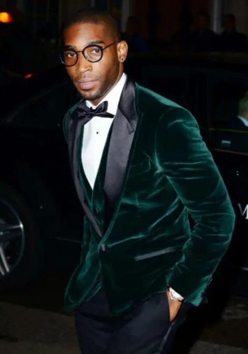 a chic fall or winter groom's outfit with a green velvet blazer with black lapels, a waistcoat, a black bow tie and pants