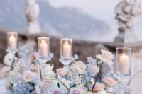 16 a fairytale wedding tablescape with blue, blush and lilac blooms, pillar candles in tall candleholders and clear chargers