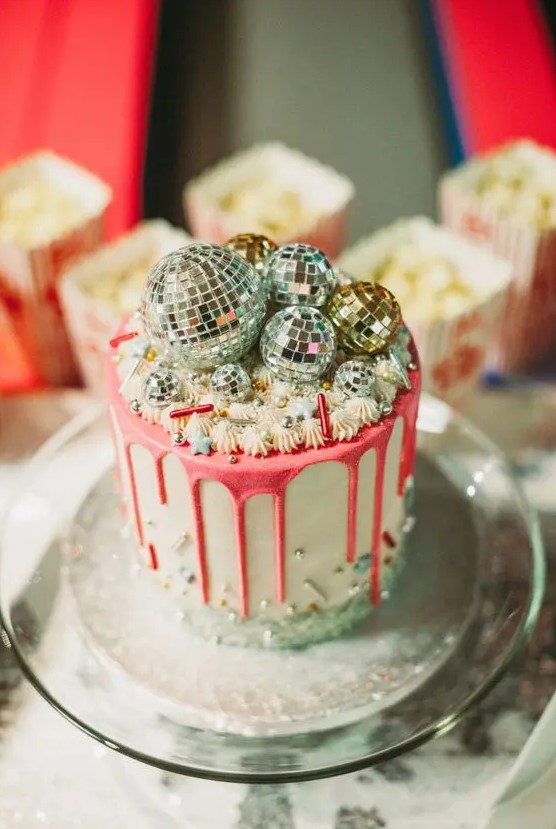 a party-themed wedding cake with pink drip, sparkles, beads and disco balls on top is a very bright idea
