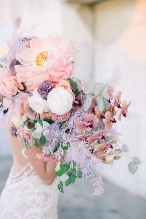 a gorgeous pastel wedding bouquet with lilac grasses, pink oversied blooms and orchids and some greenery
