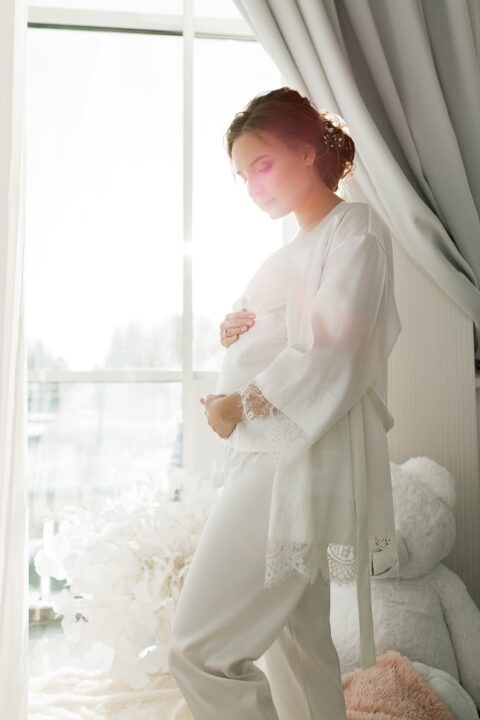 a pregnant bride wearing white pajamas with a lace edge and a matching robe over it