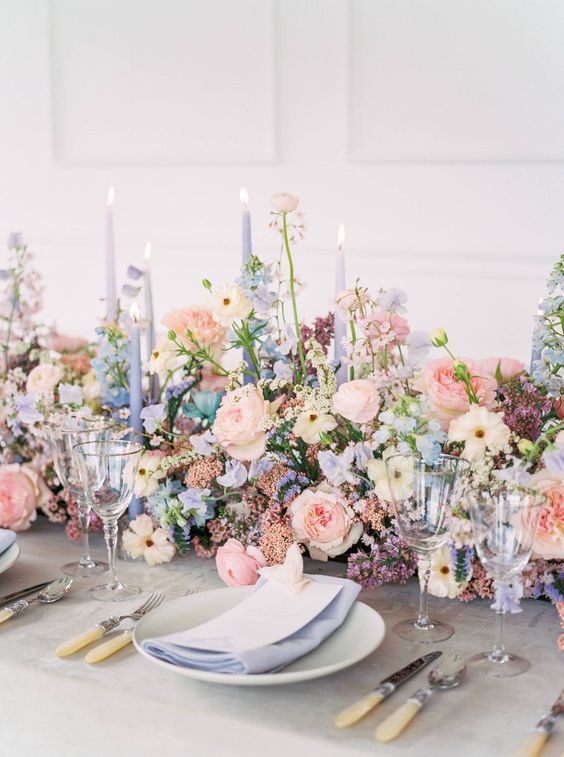 a gorgeous spring wedding tablescape with blush, blue and lilac blooms and greenery, blue and lilac candles and blue napkins