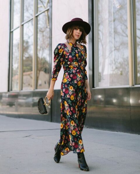 a fantastic moody floral maxi dress with puff sleeves, black boots, a purple hat and a small black bag with a round handle for a fall wedding