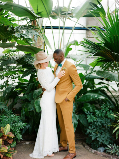 a groom wearing a mustard suit, a white shirt, a green bow tie and brown shoes looks super chic