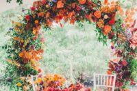 21 a super bright round wedding arch with red, orange, blue and rust blooms, greenery and dark foliage is amazing for the fall