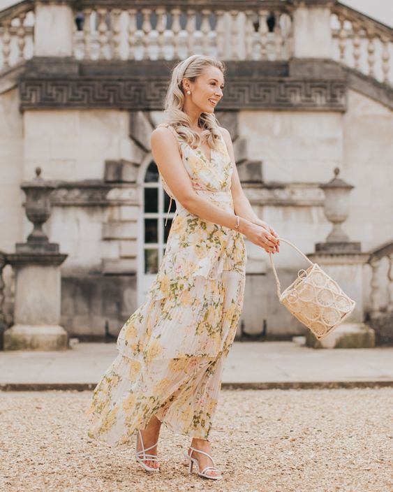 a flowy creamy maxi pleated dress with no sleeves and a V-neckline, white strappy shoes and a bucket bag for a spring wedding