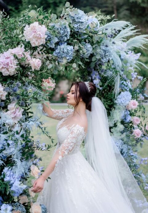 a lush spring wedding arch decorated with lush greenery, pink, blue and lilac blooms and blue pampas grass