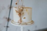 26 a white buttercream wedding cake decorated with gold leaf and dried blooms is a very refined and chic idea