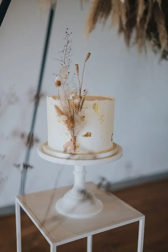 a white buttercream wedding cake decorated with gold leaf and dried blooms is a very refined and chic idea
