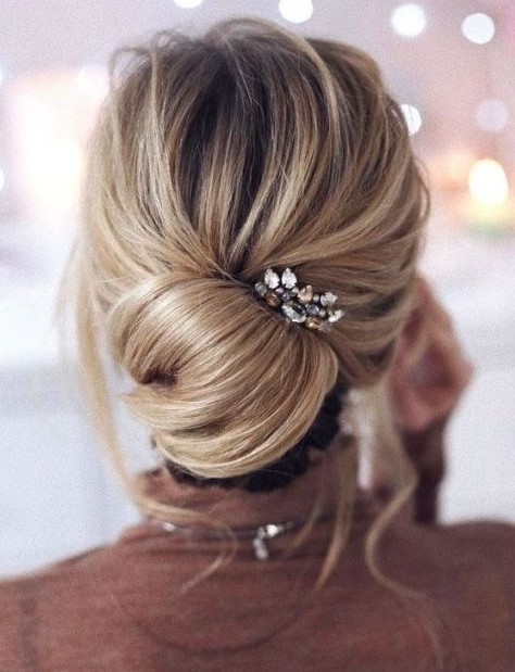 an elegant and effortlessly chic chignon with some locks down and a bump on top plus a rhinestone hairpiece