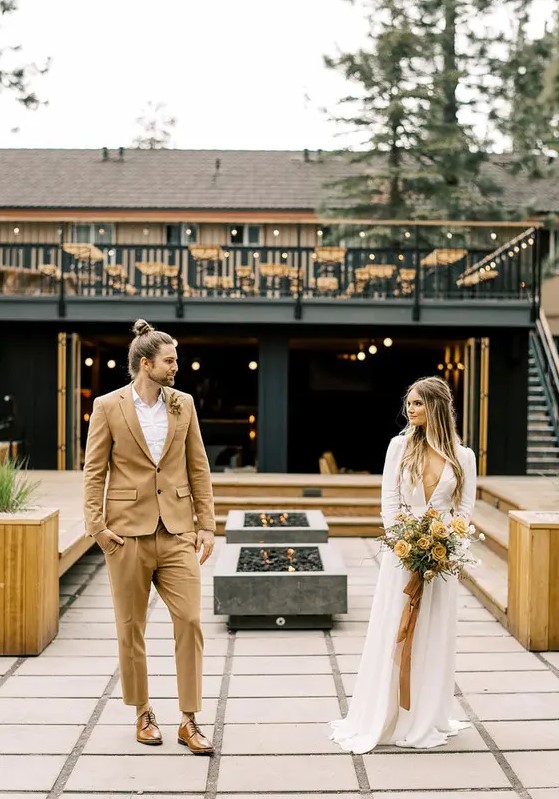 an ocher groom's suit, a white shirt, brown shoes, a dried flower boutonniere and a top knot for a boho fal wedding