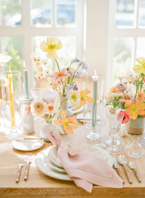 a pastel spring wedding table with pink napkins, yellow, lilac and peachy blooms, blue and yellow candles is amazing