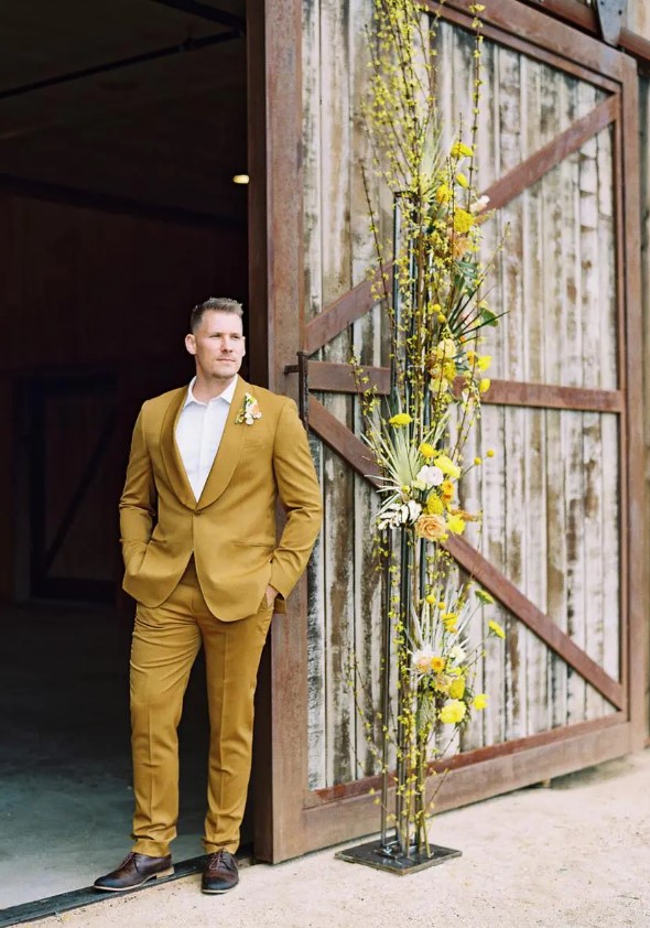 a stylish groom's look with a mustard tux, brown shoes, a white shirt and a floral boutonniere for a spring wedding