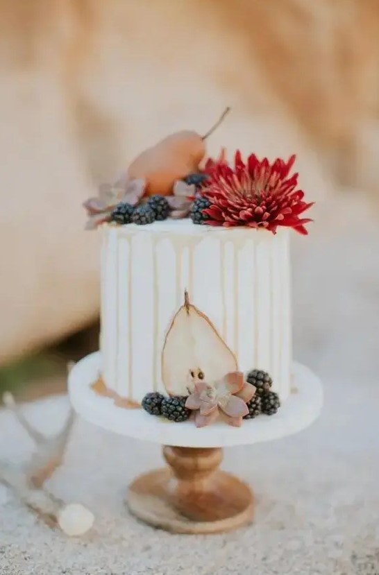 a white buttercream wedding cake with caramel drip, a bold bloom, pears and succulents, blackberries is a cool idea for the fall