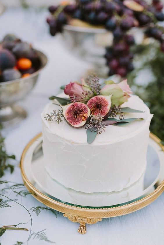 a white buttercream wedding cake with figs and pink roses on top is an elegant and stylish idea for a boho wedding in the fall
