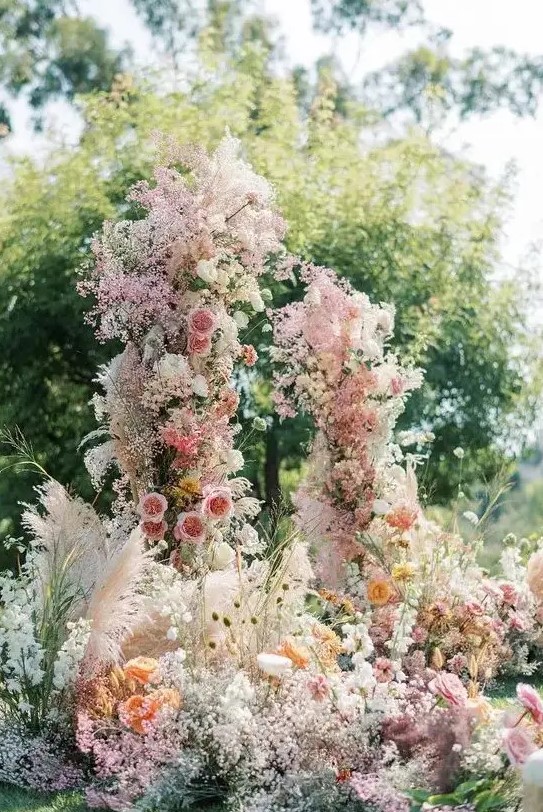 a fantastic and super lush wedding arch with pink, yellow and orange blooms and blooming branches plus pink baby's breath all over