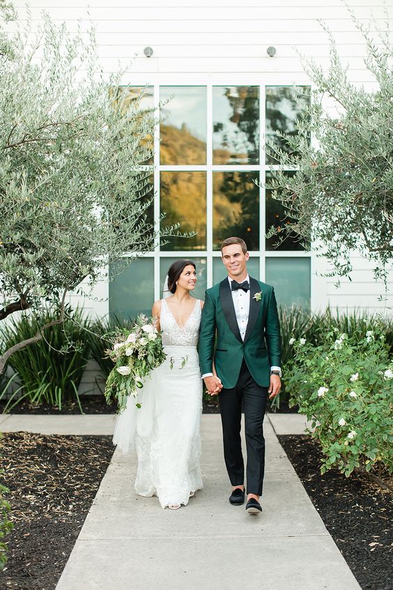 a beautiful green tuxedo with black lapels, a black bow tie, black pants and loafers compose a refined groom's look