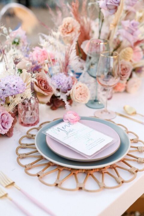 a pastel wedding tablescape with lilac, dusty pink and peachy blooms, pampas grass and rattan placemats plus pastel plates