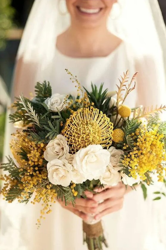 a bold yellow wedding bouquet of pincushion proteas, billy balls, mimosas, white roses and lots of greenery is wow