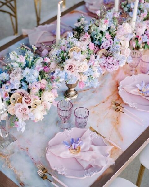 a pretty pastel wedding tablescape with refined pink plates, pastel florals, tall and thin candles and pink glasses