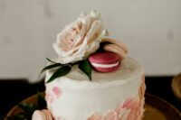 32 a white buttercream wedding cake with pink and blush sugar petals, blush and pink macarons on top, a blush bloom and leaves