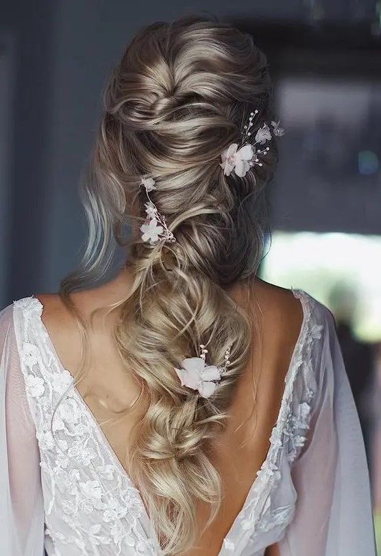 a delicate twisted and loose long ponytail with a mesys volume on top, some waves down, white blooms and beads is chic and ethereal