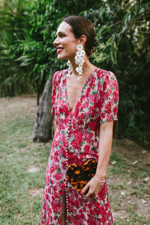 a statement summer wedding guest look with a red floral dress with buttons and short sleeves, a plunging neckline, white floral earrings and a leopard print clutch