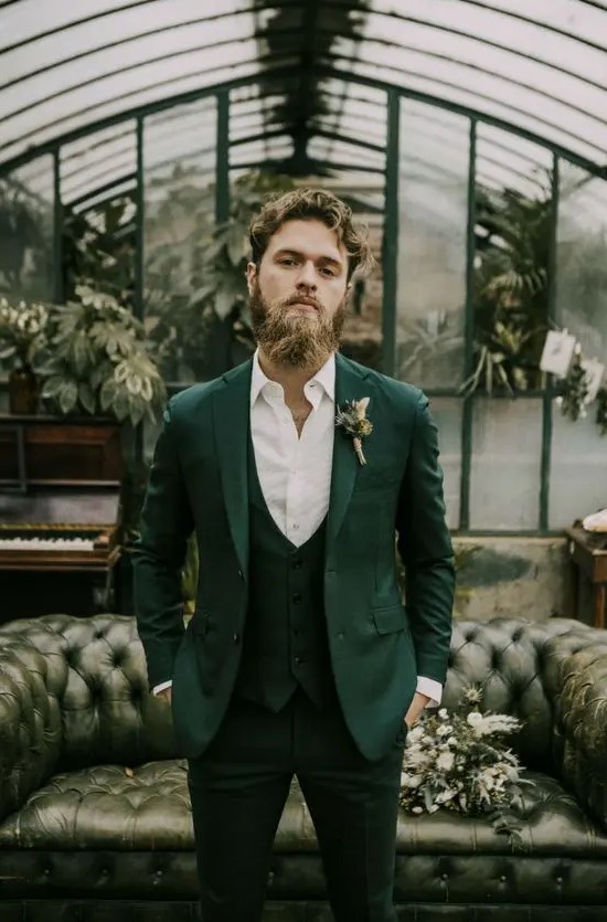 an elegant groom wearing a green three piece suit, a white shirt and a green and white boutonniere looks chic
