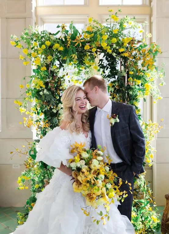 a bright wedding arch with much greenery and bold yellow blooms plus a matching wedding bouquet for spring