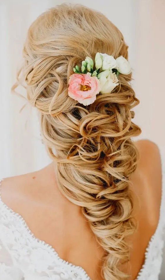 a long curly ponytail with a lot of volume and some fresh blooms tucked in is a very refined and chic idea for a bride with long hair