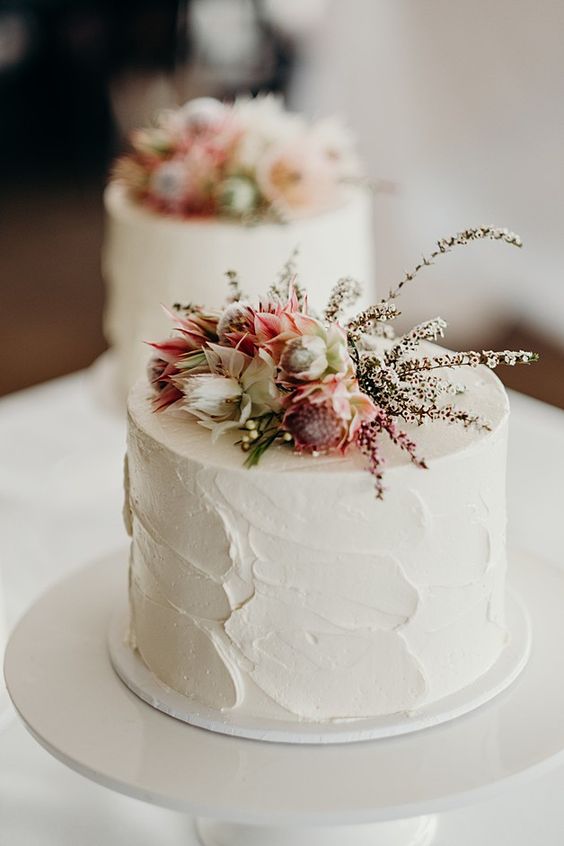a white textural buttercream wedding cake with pink and neutral blooms and twigs for a spring or summer wedding