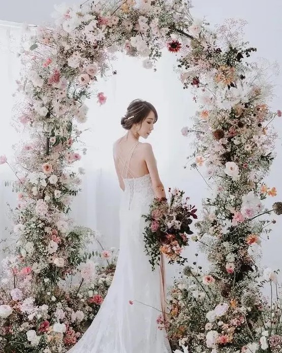 a fabulous and delicate spring wedding arch with white, blush and light pink blooms and greenery balanced with a bit of dark ones