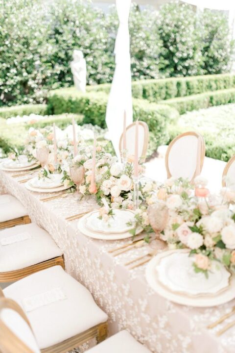 a lovely wedding tablescape with greenery, peachy and blush blooms, creamy and gold porcelain, pink glasses and blush candles