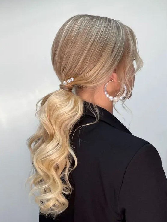 a low ponytail with waves, locks framing the face, some pearl pins and pearl earrings is a chic idea