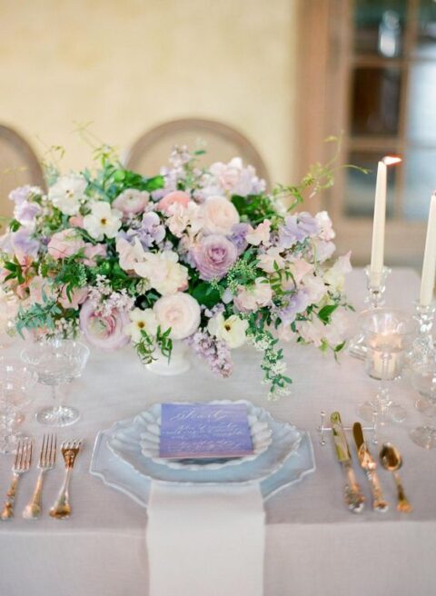 a sophisticated wedding tablescape with lilac and neutral blooms, eye-catchily shaped plates, candles and vintage glasses