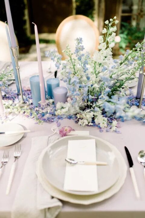a spring wedding tablescape with blue and blush candles, blue and white florals and neutral plates is chic