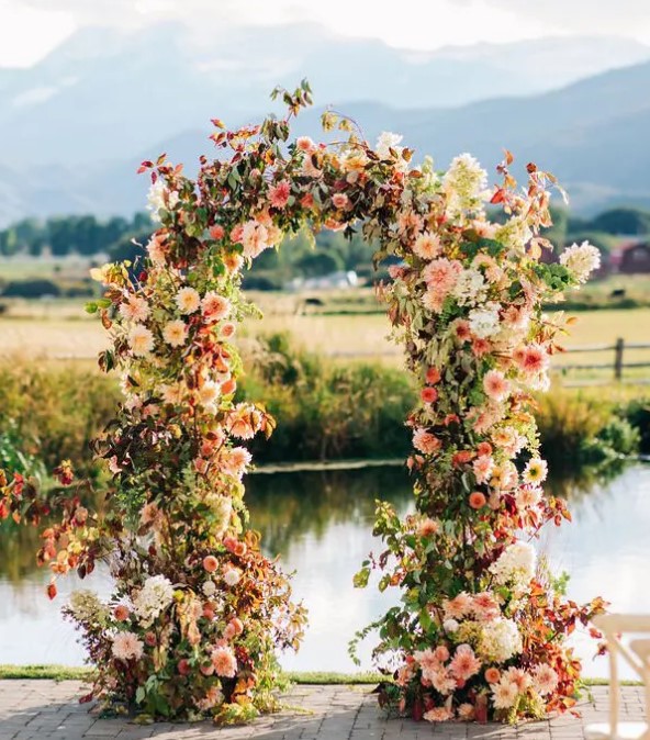 a beautiful and bright fall wedding arch of pink, blush and neutral blooms, greenery and bold foliage is a very cool and cheerful idea
