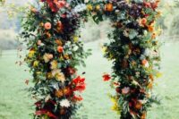 41 a beautiful and colorful rustic fall wedding arch with greenery, red, yellow, pink blooms, colorful fall leaves is a lovely idea for the season