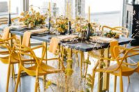 42 a contrasting modern wedding tablescape with a black table and candelholders, yellow blooms and chairs, yellow candles and yellow napkins