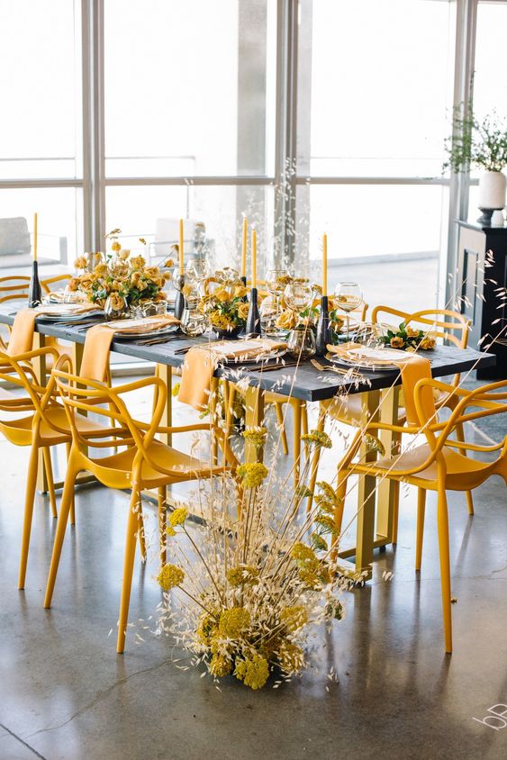 a contrasting modern wedding tablescape with a black table and candelholders, yellow blooms and chairs, yellow candles and yellow napkins