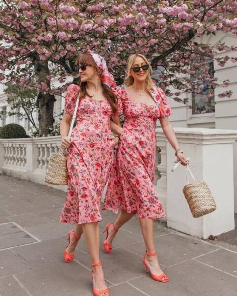 gals wearing the same pink floral midi dresses with red prints, orange shoes, straw bags for a spring wedding