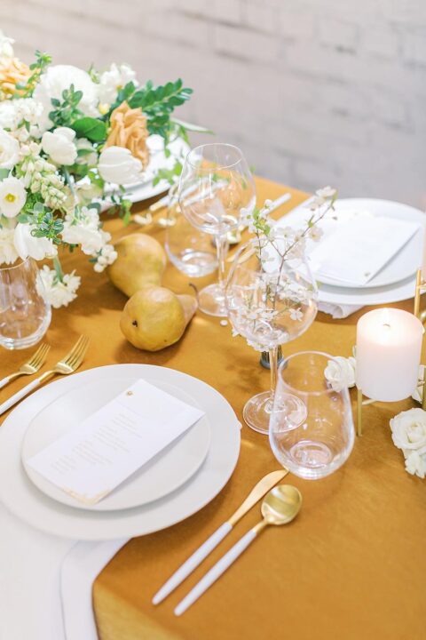 a marigold and white wedding tablescape with a bold tablecloth, blooms and pears right on the table